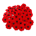 A pile of red felt poppy flowers with black centers, arranged on a plain white background.